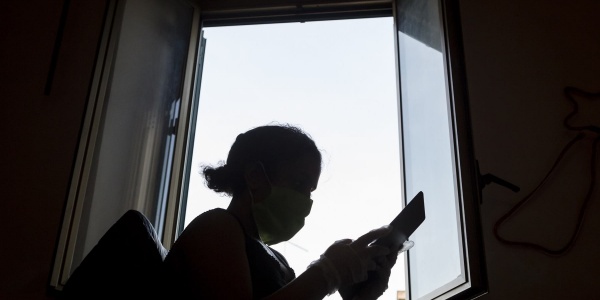 Sagoma nera in controluce di una bambina davanti a una finestra che tiene in mano un tablet e ne guarda lo schermo