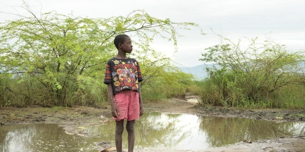 bambino a piedi nudi su un terreno fangoso dopo inondazione a causa della crisi climatica