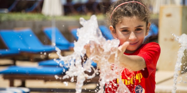 bambina bianca in primo piano con le mani tra lo spruzzo di una fontana