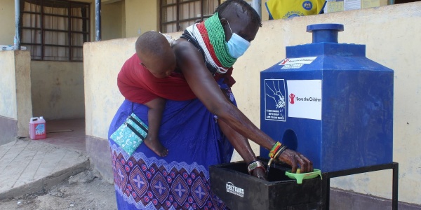 Mamma africana con bambino in fascia sulla schiena lava le mani con fontana mobile save the children.