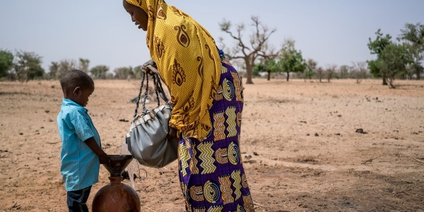 Campo lungo di madre e figlio nigeriani che si riforniscono di acqua in una terra brulla