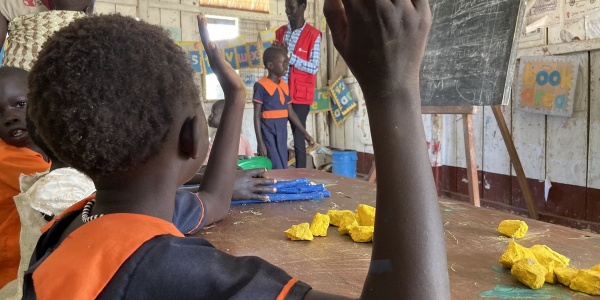 bambina ugandese di spalle con mano alzata durante lezione in classe