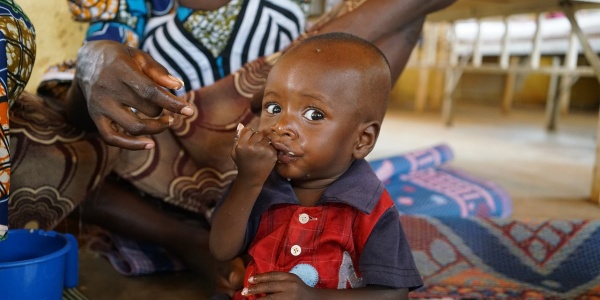 bambino nigeriano seduto a terra su un telo mangia plumpynut