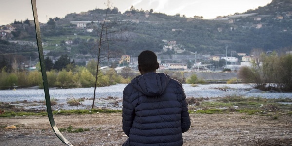 Minore straniero di spalle seduto a terra guarda panorama davanti a lui