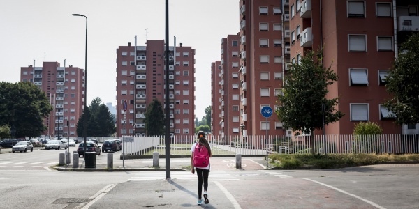 bambina di spalle cammina lungo una strada deserta a Milano tra i palazzi