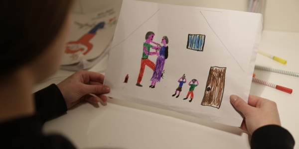 Bambina di spalle tiene in mano un disegno che rappresenta una scena di violenza domestica e assistita