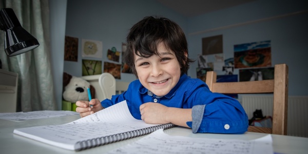 Bambino inglese seduto alla sua scrivania della camera mentre scrive su un quaderno