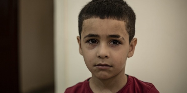 Primo piano ritratto di un bambino di circa sei anni libanese. Ha capelli corti, occhi e capelli bruni. Indossa una maglietta rossa