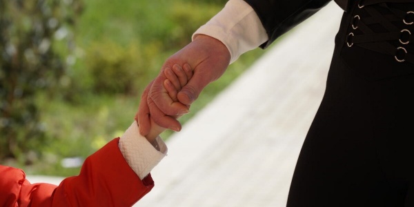mano di un bambino con la magglietta rossa che si unisce alla mano della madre con maglietta nera su sfondo di un giardino