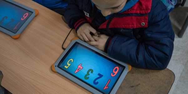 bambino seduto al banco studia con un tablet davanti