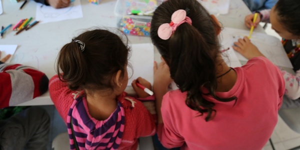 due bambine di spalle al banco di scuola che disegnano