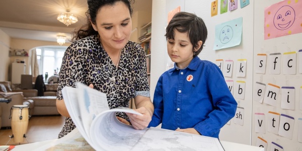 mamma e figlio sfogliano libro con sfondo di una casa e di una libreria con disegni fatti dal bambino