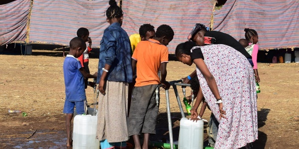 un gruppo di bambini e ragazzi etiopi in un campo per rifugiati si affollano intorno a una fonte d'acqua per raccoglierla con le taniche