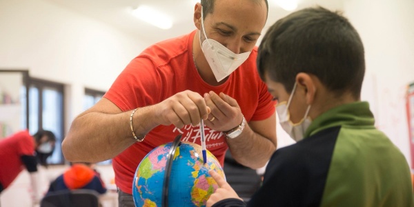 Operatore Save the Children mostra un dettaglio sul mappamondo a un bambino seduto di fronte a lui.