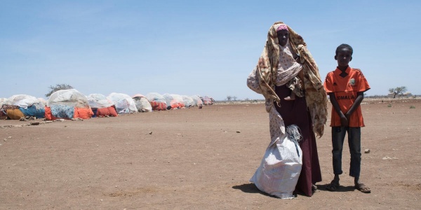 Madre e figlio fuori da un campo profughi in Somalia su terra arida con un sacco di yuta bianco
