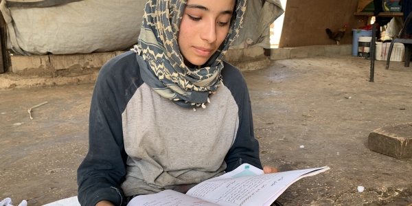 Ragazza palestinese con kufia in testa è seduta a terra e legge un quaderno che tiene poggiato sulle ginocchia