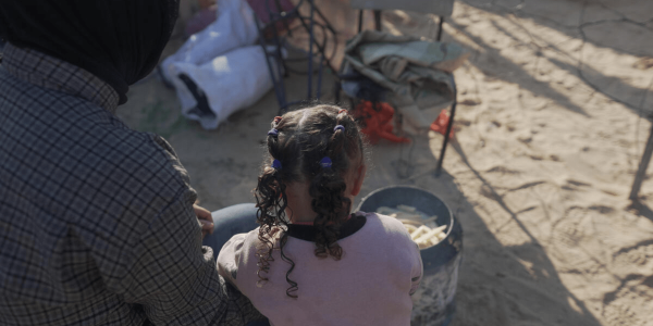 bambina a Gaza con accanto madre che guarda una pentola con cibo 