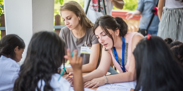 due educatrici e tre studenti sono seduti a un banco di scuola a fare attività educative insieme