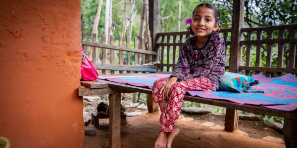 bambina seduta su un letto di legno in un patio vestita colorata con le treccine