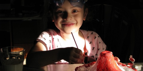 bambina sorridente con maschera snorkeling sulla fronte seduta al tavolo tiene in mano un pennello mentre lavora a un esperimento