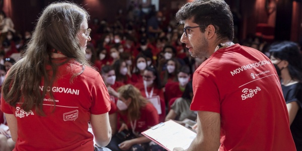 Un ragazzo e una ragazza con la maglietta rossa del movimento giovani di Save the Children discutono su un palco di fronte ad una platea di giovani