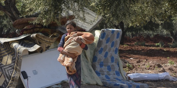 Bambina siriana attraversa campo sfollati con in braccio neonato