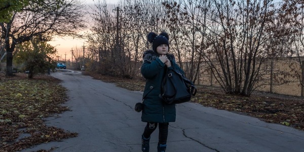 Una bambina ucraina vestita di blu con cappello di lana cammina su una strada in cemento alberata