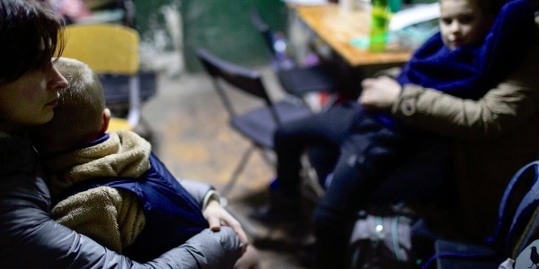 Una mamma ucraina di profilo tiene in braccio il suo bambino da seduta all interno di una stanza con altre persone sedute.