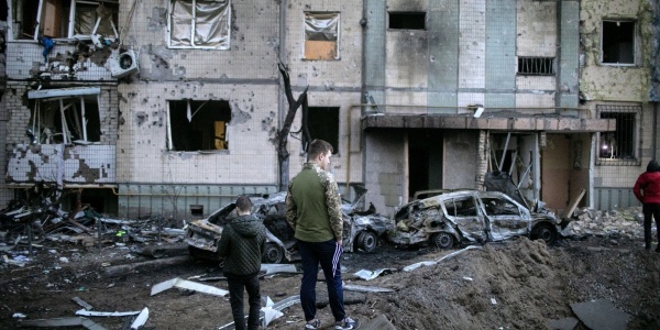 Ucraina, un bambino e un ragazzo in piedi di spalle davanti a edifici e macchine distrutti e in macerie a causa dei bombardamenti