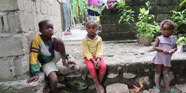 Tre bambini haitiani seduti su un gradino guardano in camera