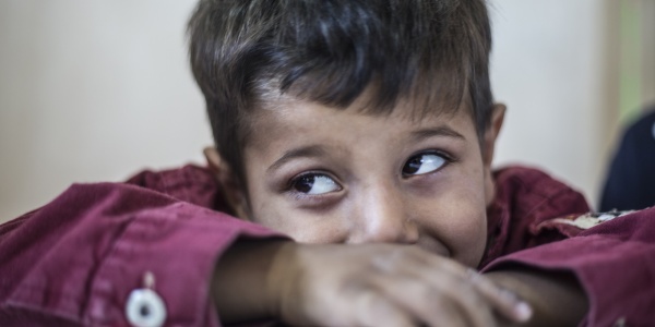 Bambino al tavolo, primo piano, alza gli occhi a sinistra sorridendo