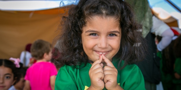 Foto mezzo busto bambina riccia con fiocco azzurro in testa e con le mani giunte davanti alla bocca