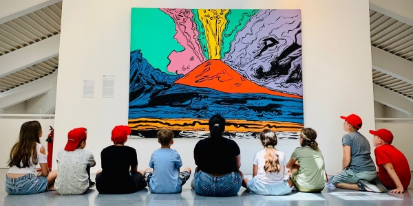studenti e studentesse seduti a terra mentre guardano un quadro di un vulcano