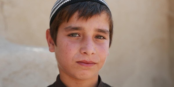 primo piano di un bambino afgano con cappello tradizionale e bianco e nero 