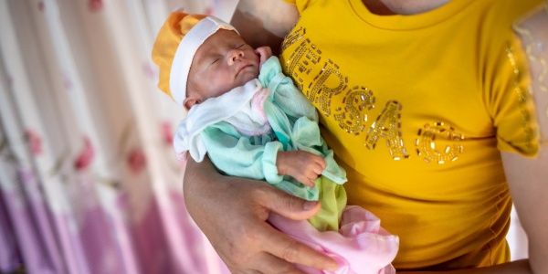 neonato con berrettino e tutina in braccio ad una donna