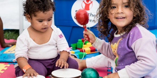 due bimbe piccole sedute per terra su un tappetino giocano con degli strumenti musicali per bimbi