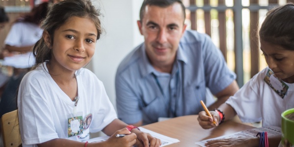 uomo adulto tra due bambine seduti a un tavolo a colorare e disegnare insieme, tutti sorridenti