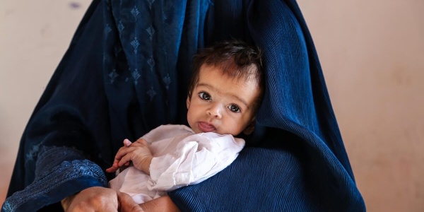 una bambina neonata in braccio alla sua mamma con un vestito turchese indossa un abitino bianco e guarda in camera