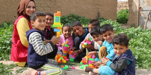 bambini afghani seduti a terra in cerchio mentre giocano sorridenti alle costruzioni insieme a operatrice save the children 
