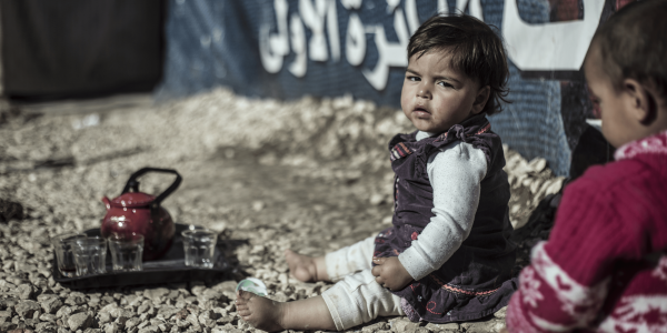 Bambina in Libano seduta per terra a piedi nudi e con lo sguardo triste