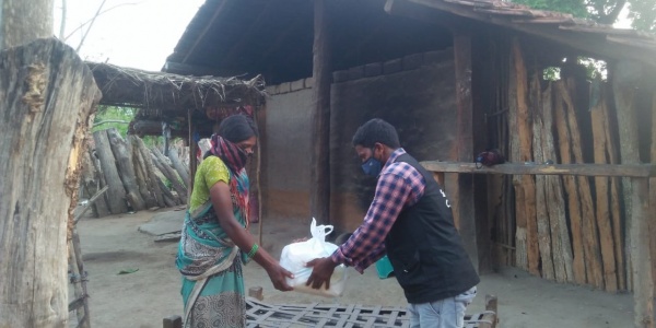 Un operatore save the children distribuisce cibo a una donna indiana, sullo sfondo una casa di legno