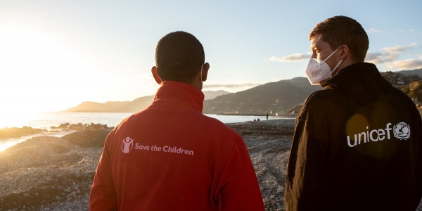 Due operatori, uno save the children e l altro Unicef, di spalle guardano un tramonto davanti a loro.