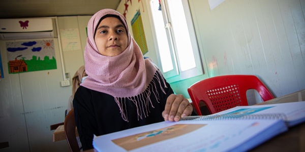 Bambina con chador rosa è seduta a un banco con il libro davanti