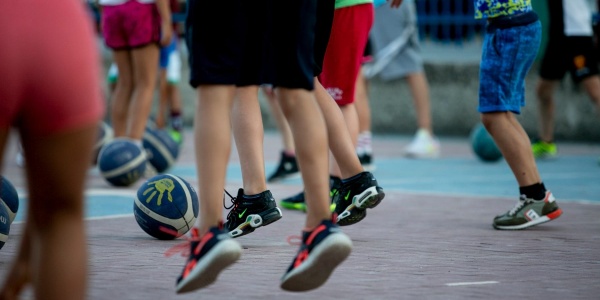 Primo piano di gambe di bambini e bambine che giocano con la palla in un campo da basket