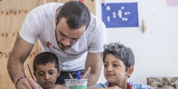 operatore umanitario in piedi aiuta due bambini seduti al banco di scuola a fare i compiti