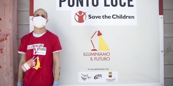 Un operatore save th children posa davanti al cartello di ingresso del Punto Luce di Napoli Barra.