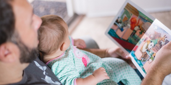 bimba neonata in braccio al papà mentre leggono insieme un libro illustrato