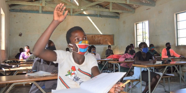 Bambina dello Zambia con la mascherina seduta al banco in classe con mano alzata