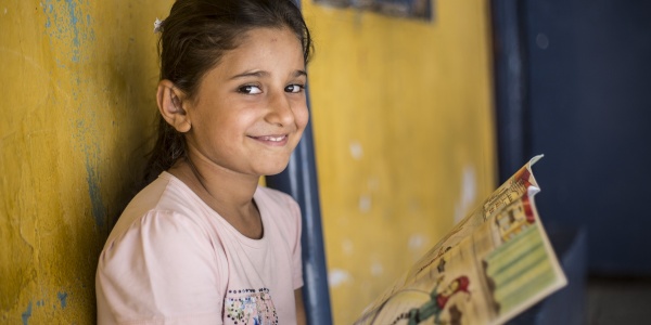 Bambina sorridente guarda in camera mentre tiene in mano un libro aperto e colorato