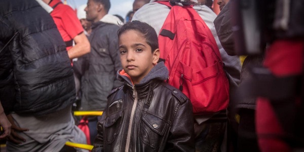 bambino che guarda dritto in camera mentre è circondato la persone